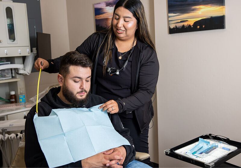A staff member helping a patient with a bib in an exam chair at Pocock Family Dental in Twin Falls ID.